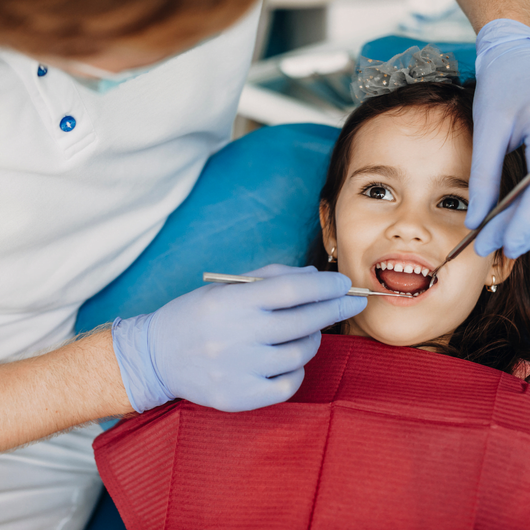 Niña en su primera visita al dentista, explorada con el espejo dental