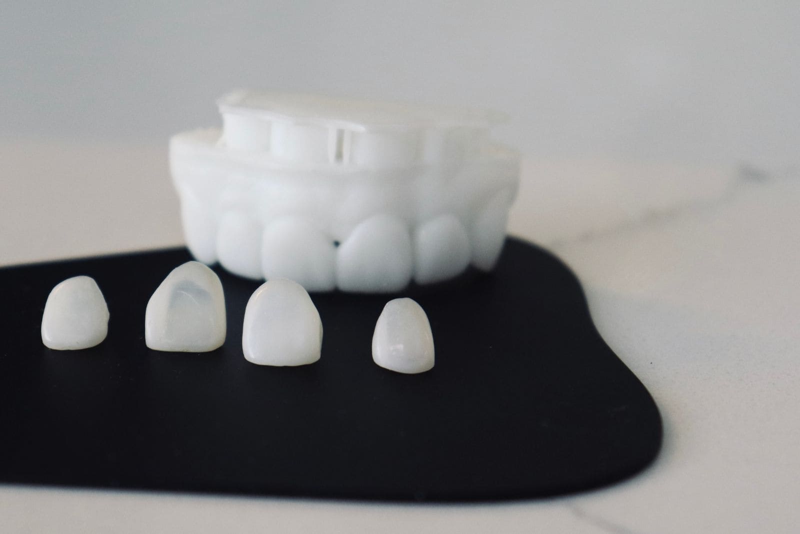 Four zirconia veneers on a black background, in front of a model of the upper arch