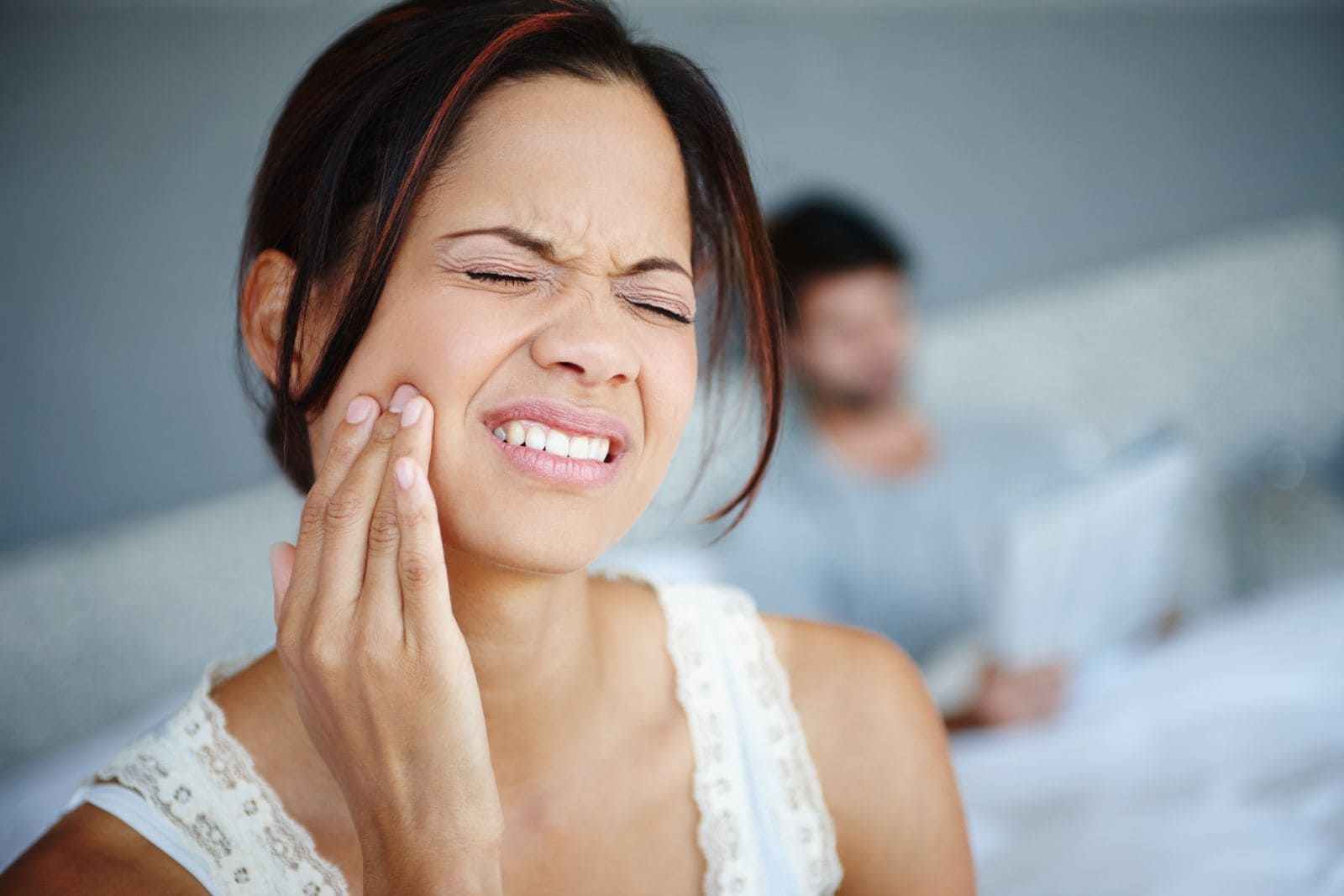 Woman wincing in pain and holding her jaw on waking up