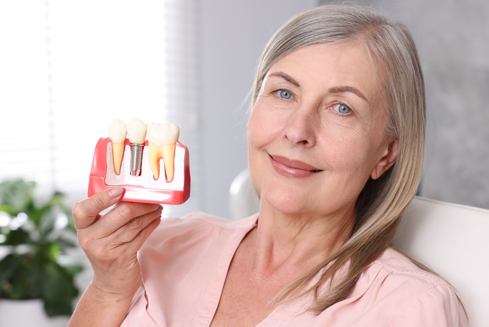 Mujer mayor sonriente sosteniendo un modelo de implantes dentales