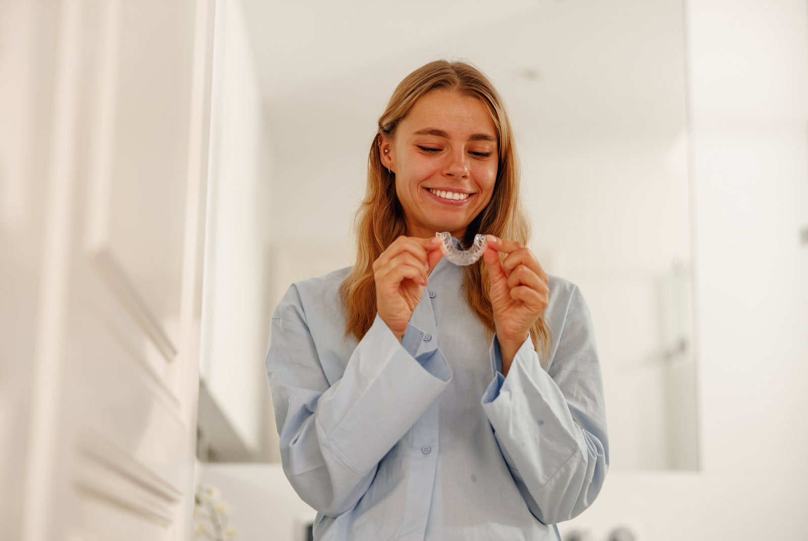 Mujer sonriente sosteniendo sus alineadores transparentes en casa