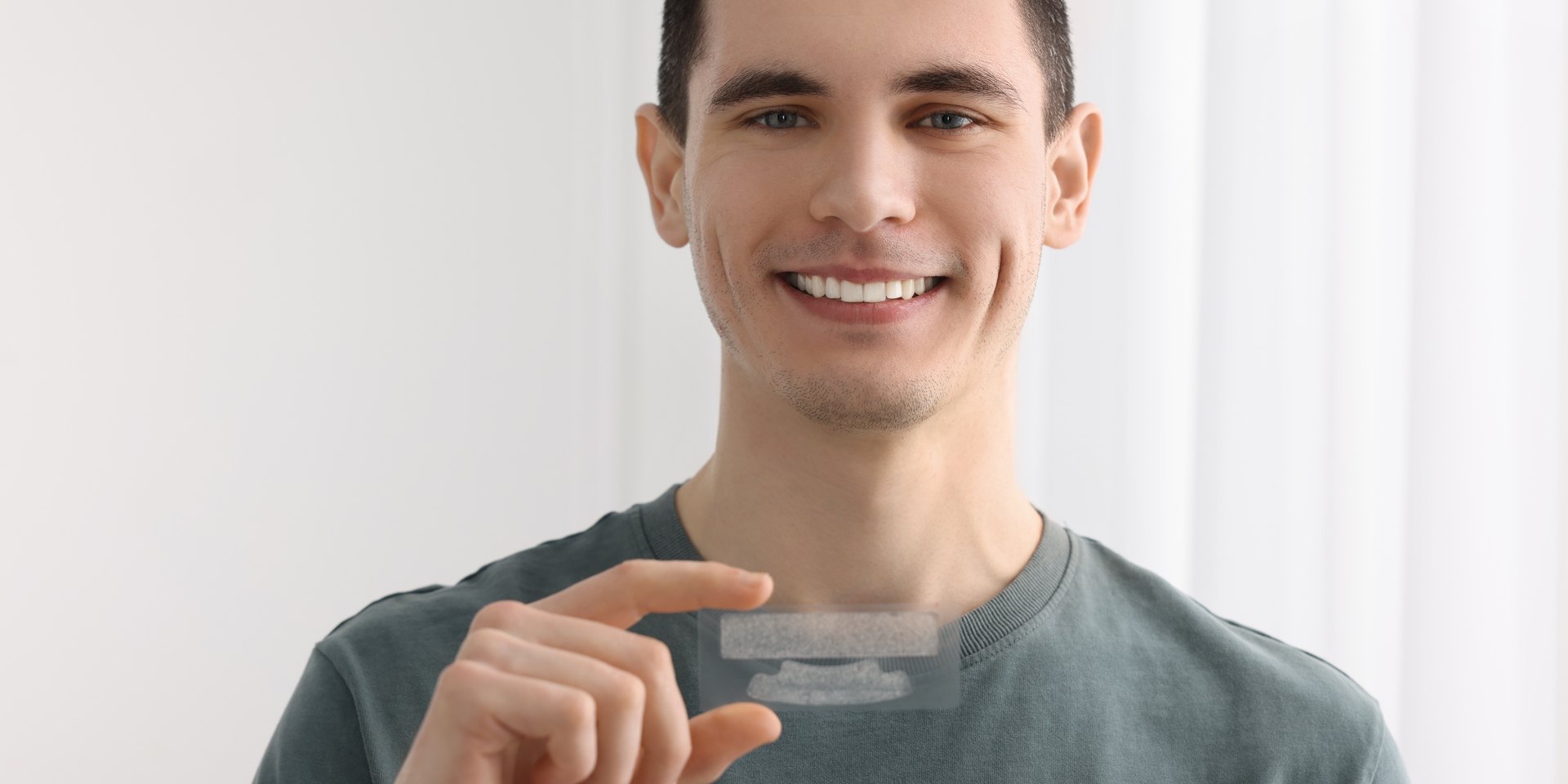Hombre joven sonriente sosteniendo una tira blanqueadora dental