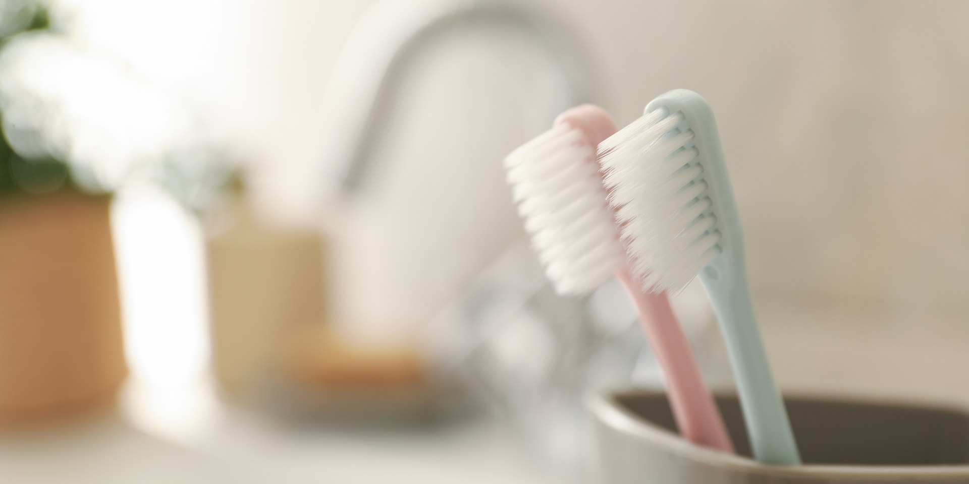 Dos cepillos de dientes de colores suaves, rosa y azul, en un vaso junto al lavabo