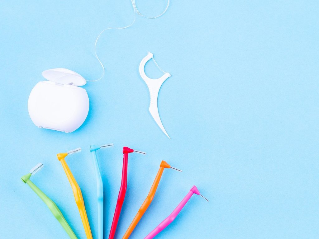 Hilo dental, un palillo con hilo y cepillos interdentales de varios tamaños sobre fondo azul