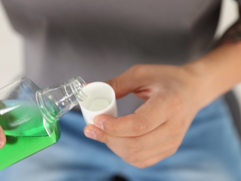 Manos echando enjuague bucal de la botella al tapón dosificador