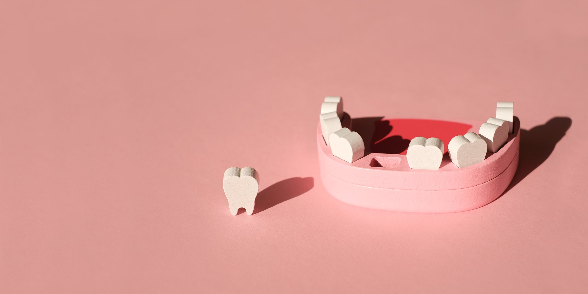 Maqueta de madera de una boca con dientes de leche y un diente caído al lado, sobre fondo rosa