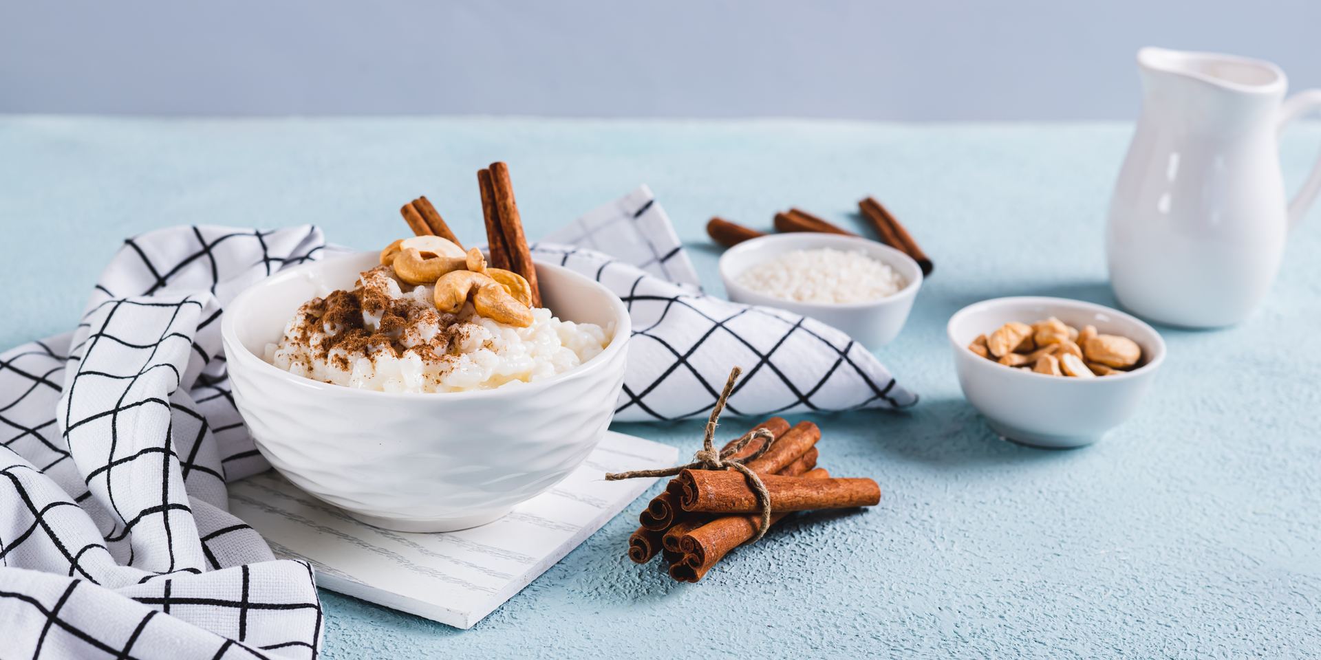 Bol de arroz con leche, cuenco de arroz y jarra de leche sobre una mesa clara