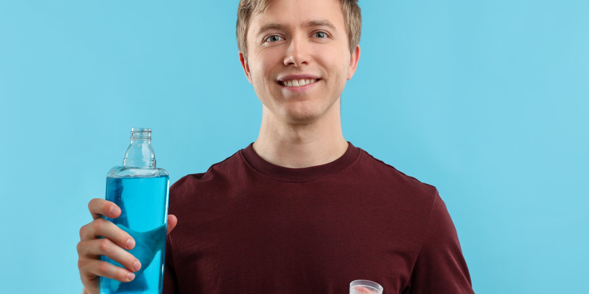 Hombre sonriente con una botella de enjuague bucal y el vaso dosificador en la mano