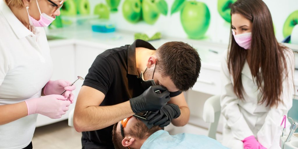 Dentista con lupas de aumento atendiendo a un paciente en el sillón, junto a dos asistentes con mascarilla