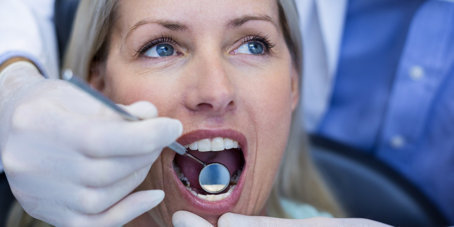 Dentista revisando con un espejo dental los dientes de una paciente en la consulta