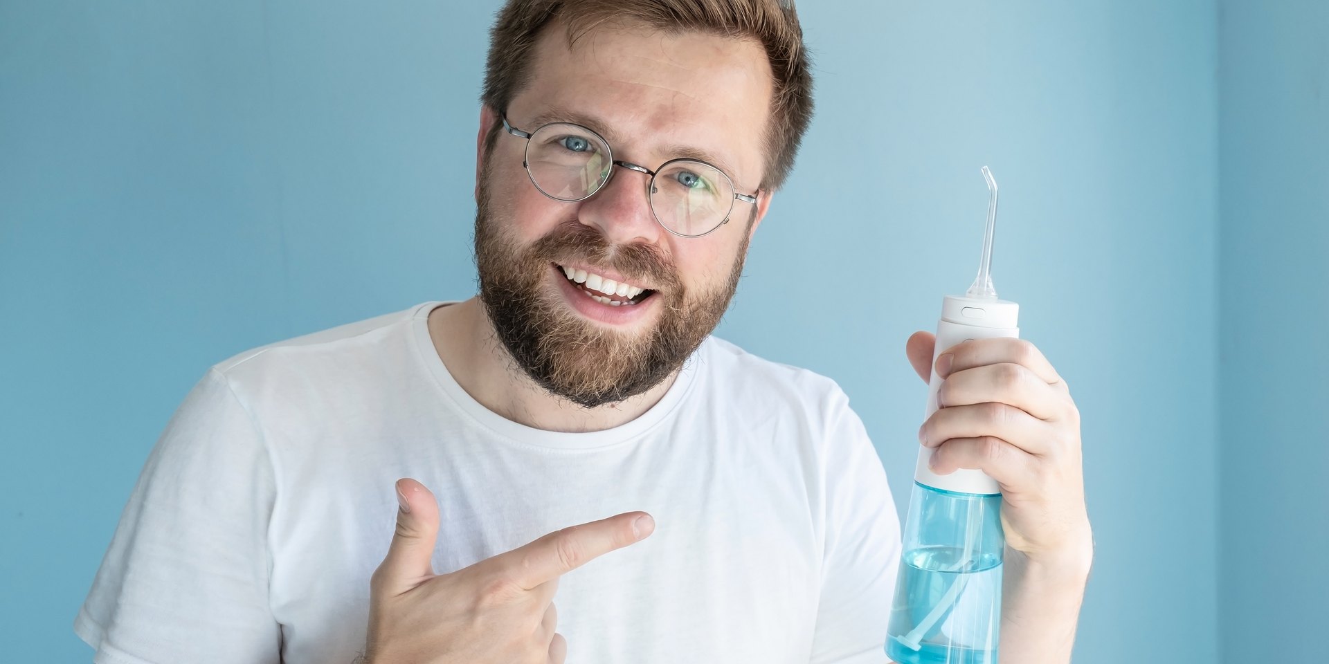 Hombre sonriente señalando el irrigador dental portátil que sostiene en la mano