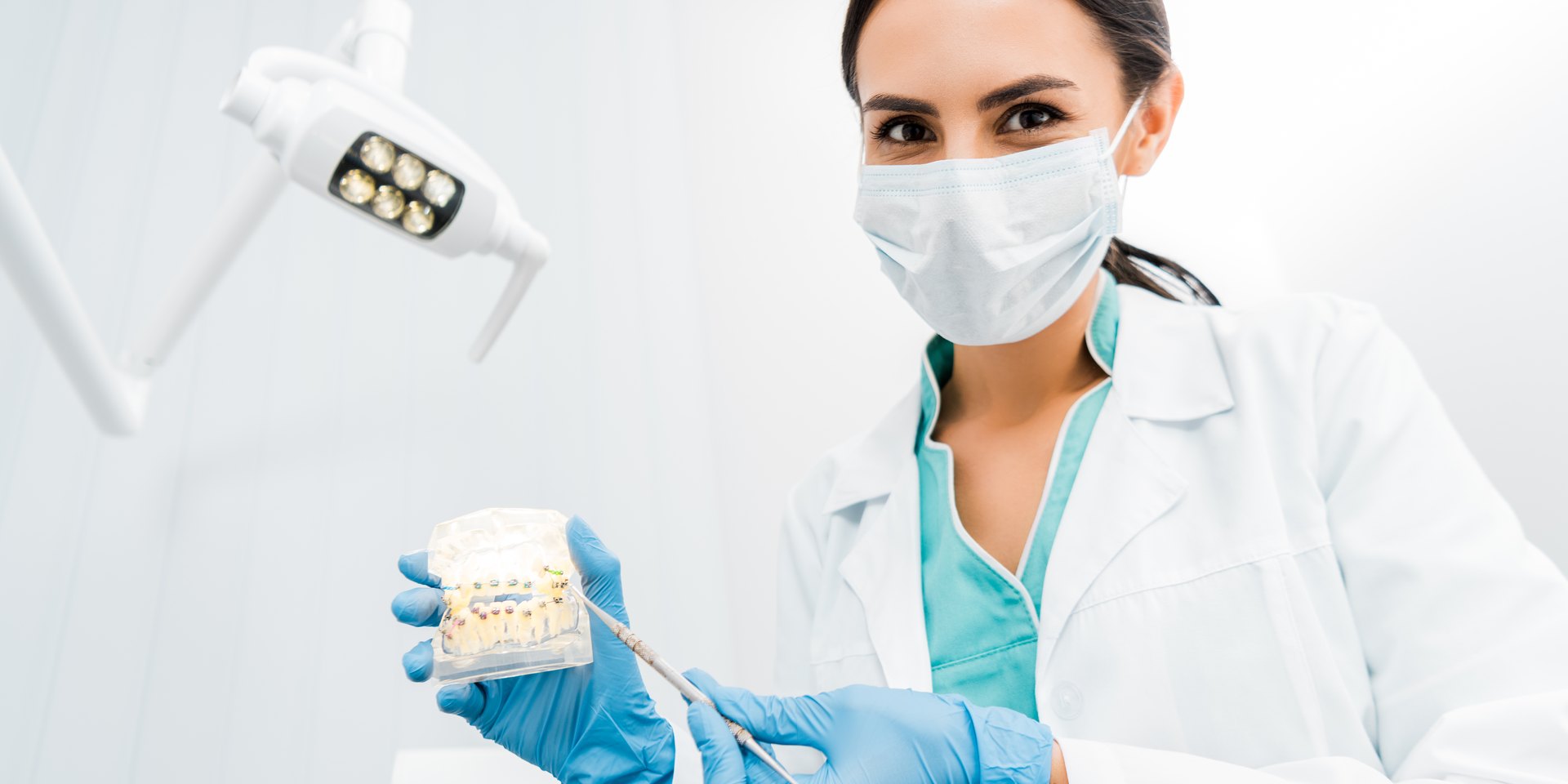 Dentista con mascarilla enseñando un modelo dental con brackets en la consulta