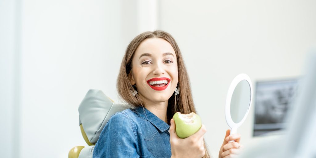 Paciente sonriente en el sillón dental que se mira en un espejo de mano