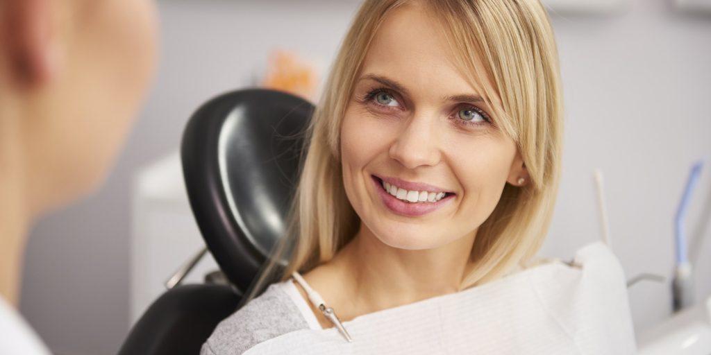 Mujer sonriente y relajada sentada en el sillón dental, mirando a la persona que la atiende