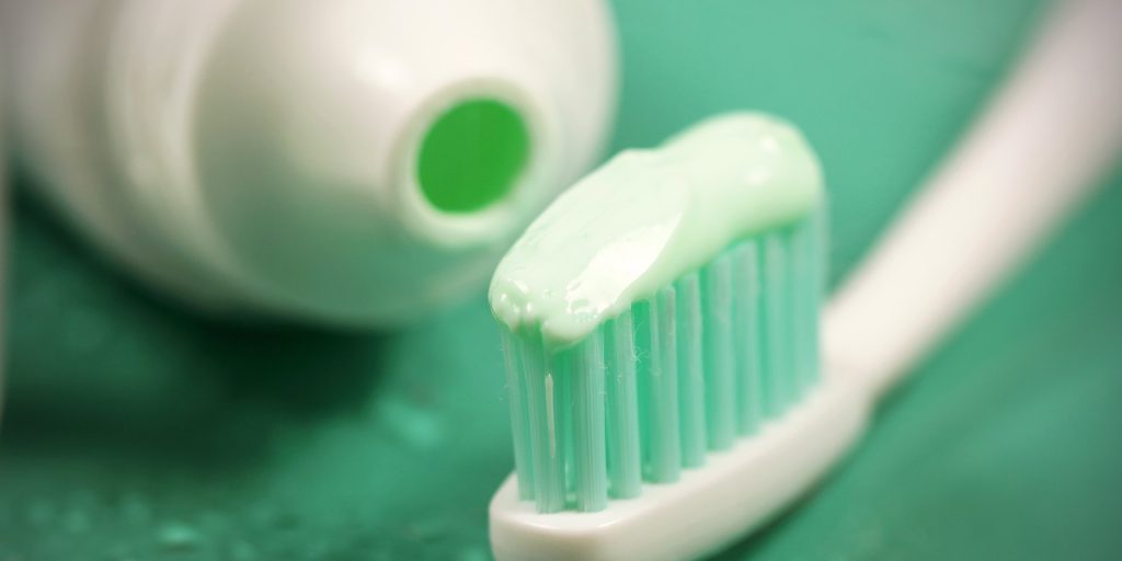 Cepillo de dientes con pasta de flúor junto al tubo abierto