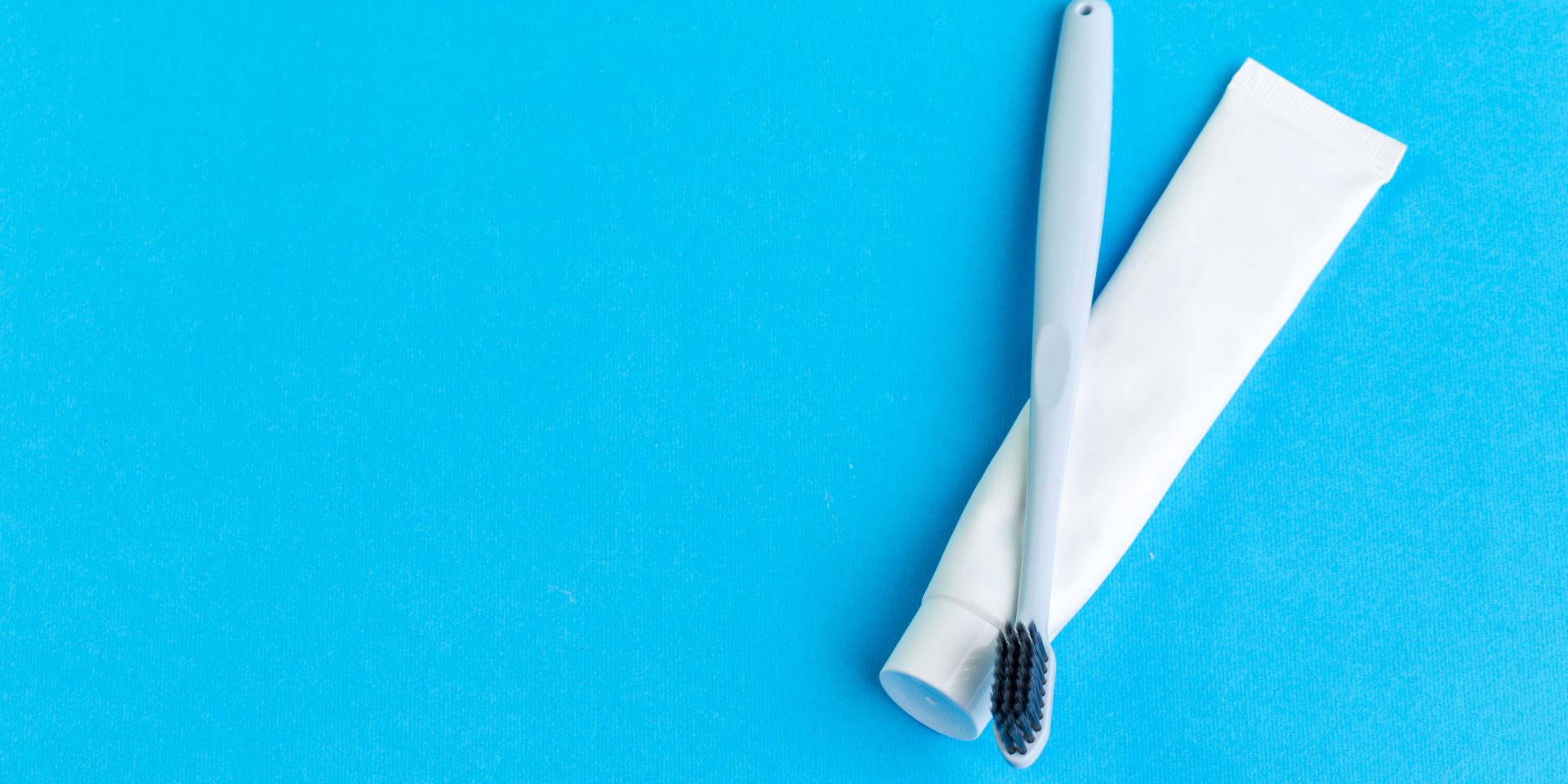 Cepillo de dientes y tubo de pasta de dientes sobre fondo azul