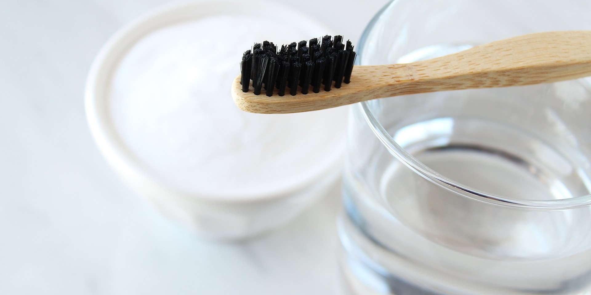 Cepillo de dientes de bambú sobre un vaso de agua junto a un cuenco de bicarbonato