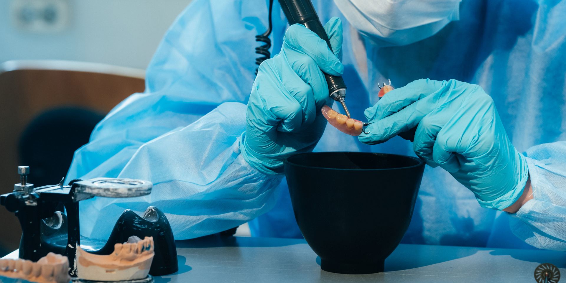 Técnica dental con guantes y mascarilla que repasa una dentadura postiza parcial en el laboratorio