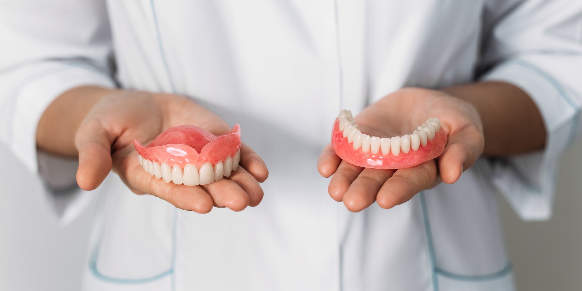 Dentista con bata blanca que sostiene una dentadura postiza superior y otra inferior en las manos