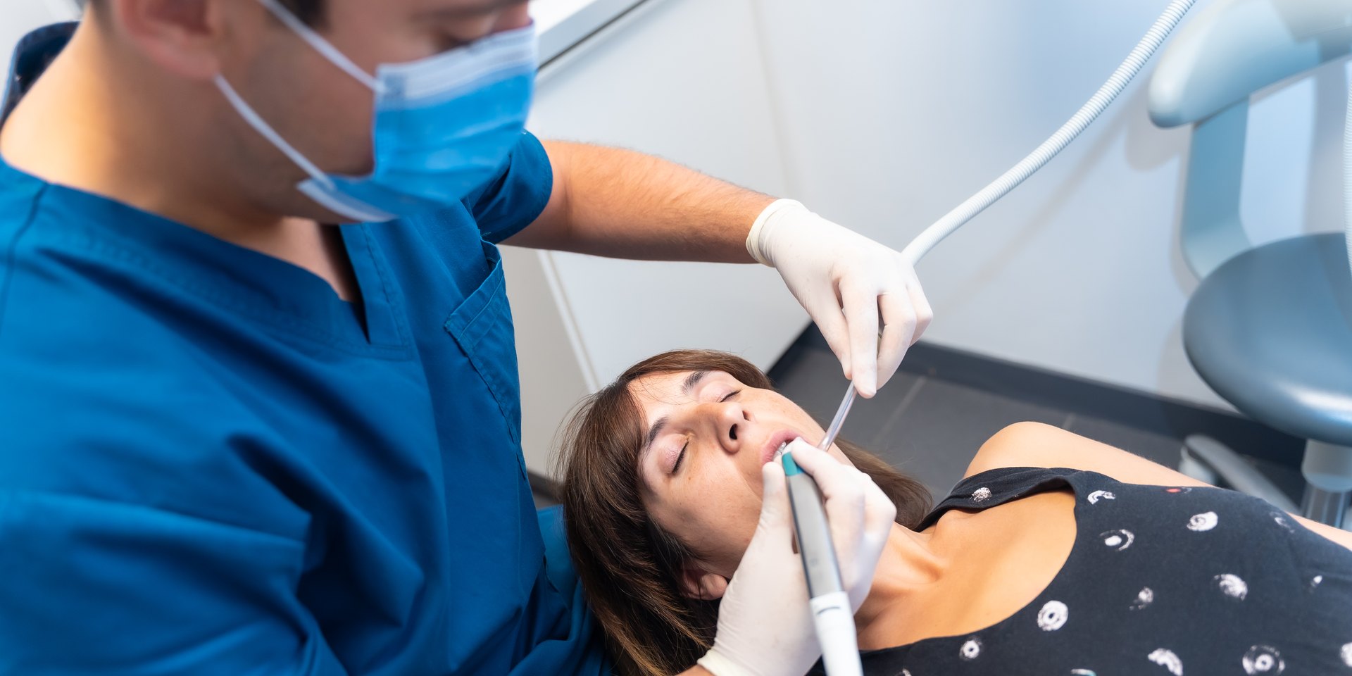 Dentista con mascarilla haciendo un empaste a una paciente tumbada en el sillón dental
